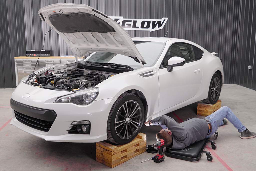 Riley from XKGLOW underneath a white Subaru BRZ, installing underglow.