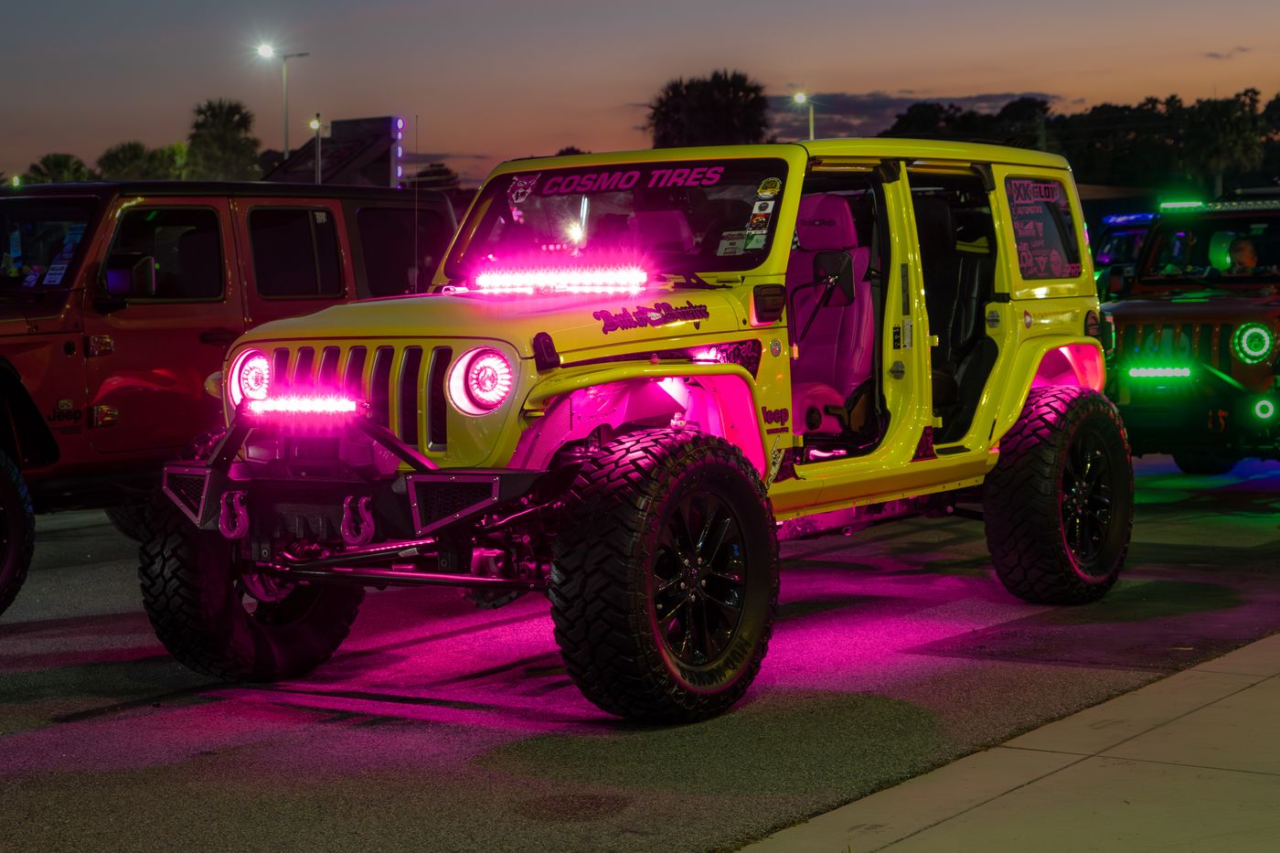 Yellow Jeep Wrangler at a night meet with pink rock lights, a pink light bar, and halo headlights