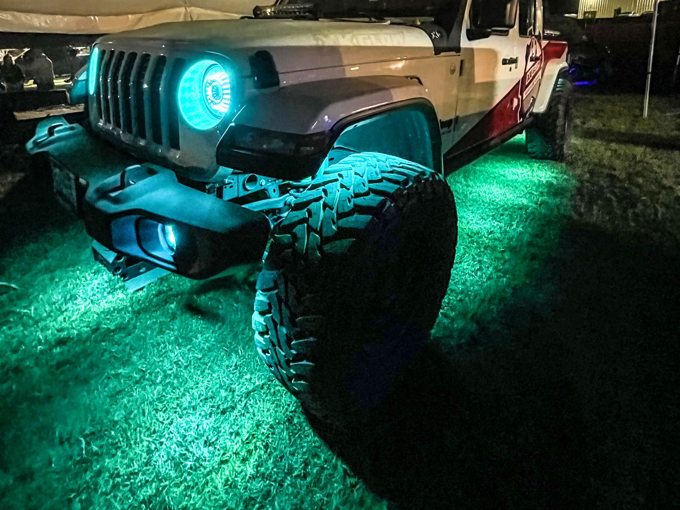 Jeep Gladiator at a night campsite with teal rock lights and a teal halo headlight