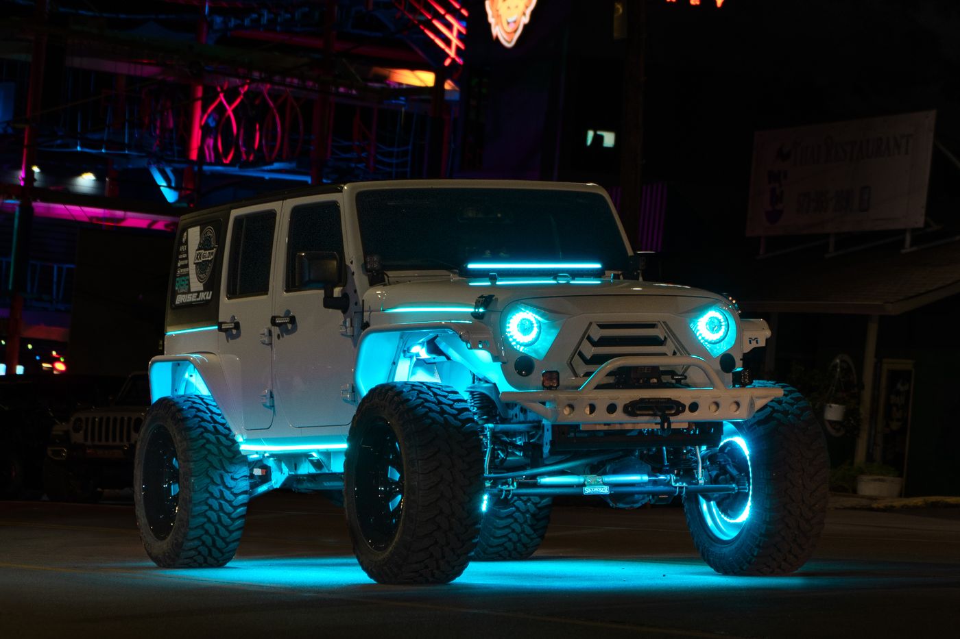 Jeep Wrangler with teal halo headlights and blue underglow on a city street at night