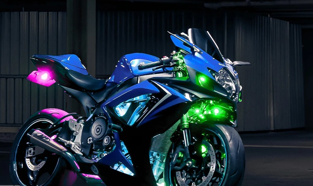 Blue sport motorcycle at night with green lights at the front fairing and pink lights at the tail and rear wheel
