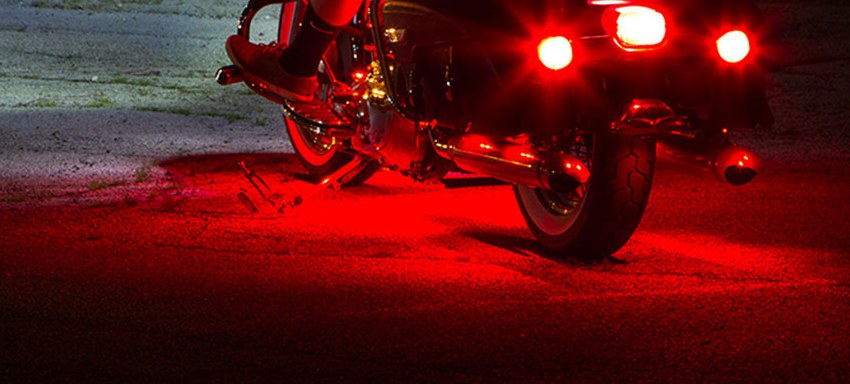 Rear of a motorcycle at night with red brake lights lit and a red glow spread across the pavement beneath it