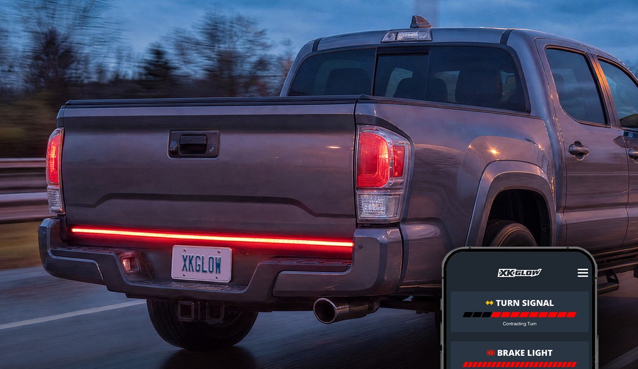 Gray pickup tailgate with a red LED light bar glowing at dusk, with a phone showing the app's turn signal settings
