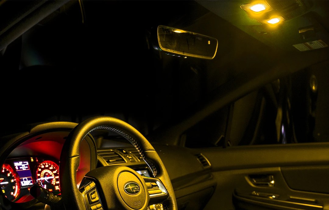 Vehicle interior in the dark with amber light on the steering wheel and two amber dome lights glowing overhead