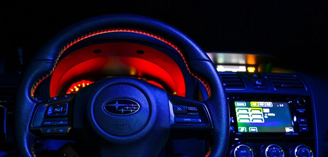 Steering wheel and dashboard in the dark, lit blue, with a red glow around the gauge cluster and a touchscreen at right